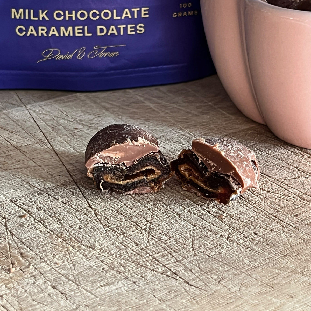 Dave & Jon's Drips milk chocolate caramel date cut in half showing the soft date centre and chocolate shell, with the 100 g pack behind